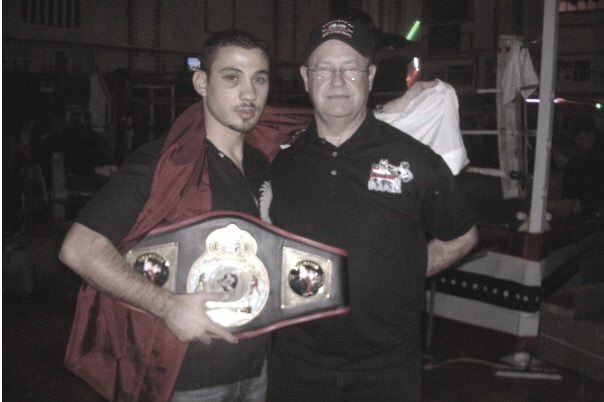 Rami Al Banna holding a championship belt, standing beside an official.