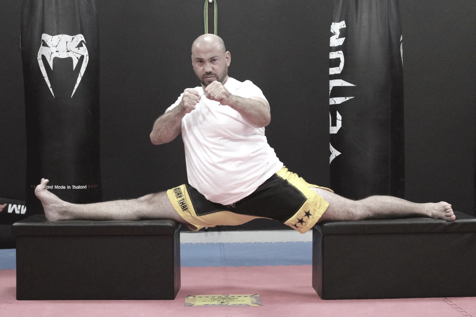A coach holding a full box splits between two benches in the gym, a VENUM banner behind him.