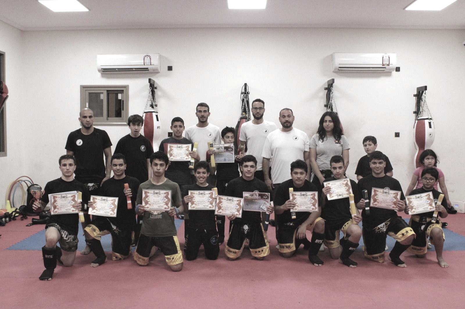 A class of children kneeling in a row on the mat, each holding a certificate, coaches standing behind them.
