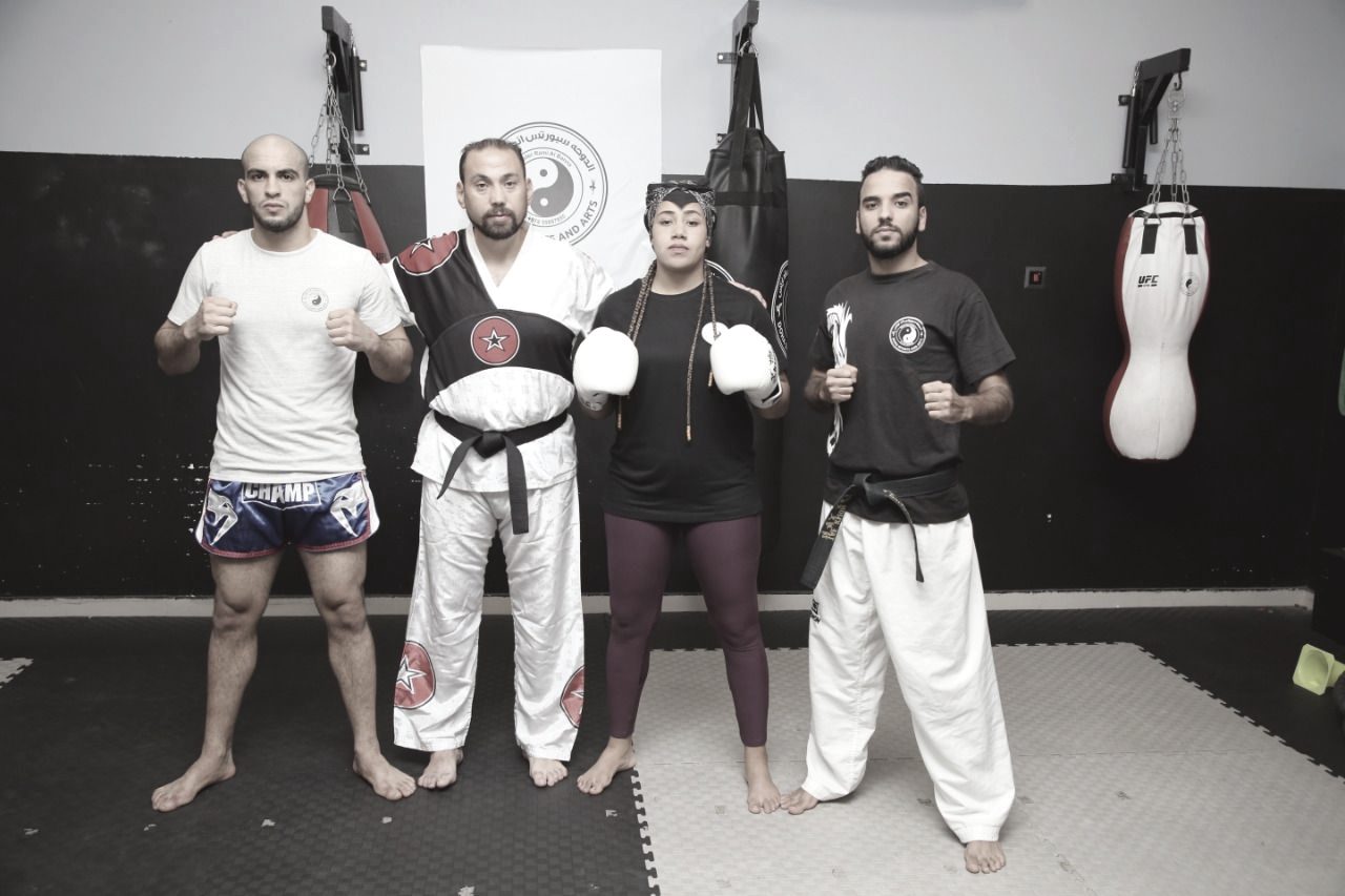 Four Doha Sports and Arts coaches standing together in gloves and training kit in front of the club's punching bags, one of them a woman.