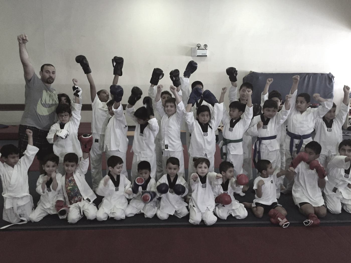 Children in white martial arts uniforms cheering with arms raised after a class.