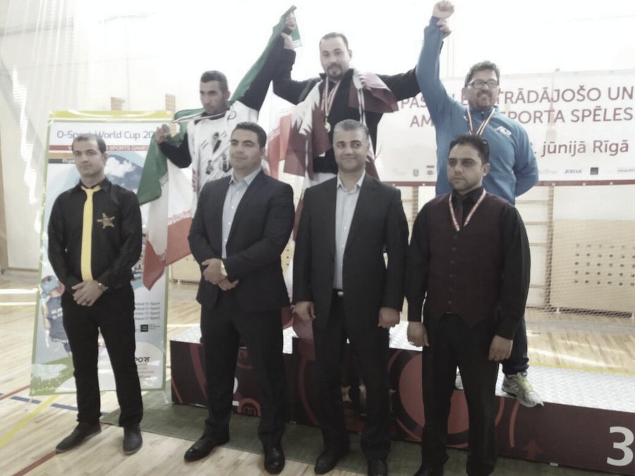 A group of men with arms raised in front of a banner for an international sports meet in Riga.