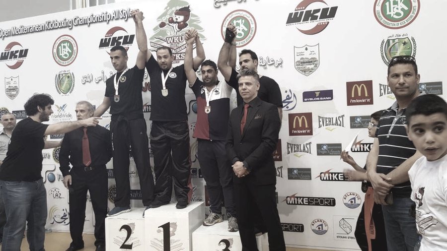 Rami Al Banna on the top step of a podium with other medallists, a WKU branded backdrop behind them.