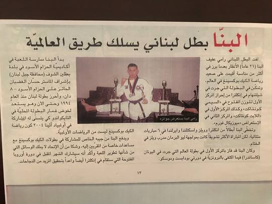 An Arabic newspaper cutting with a photograph of Rami Al Banna in a white gi surrounded by trophies and wearing medals.