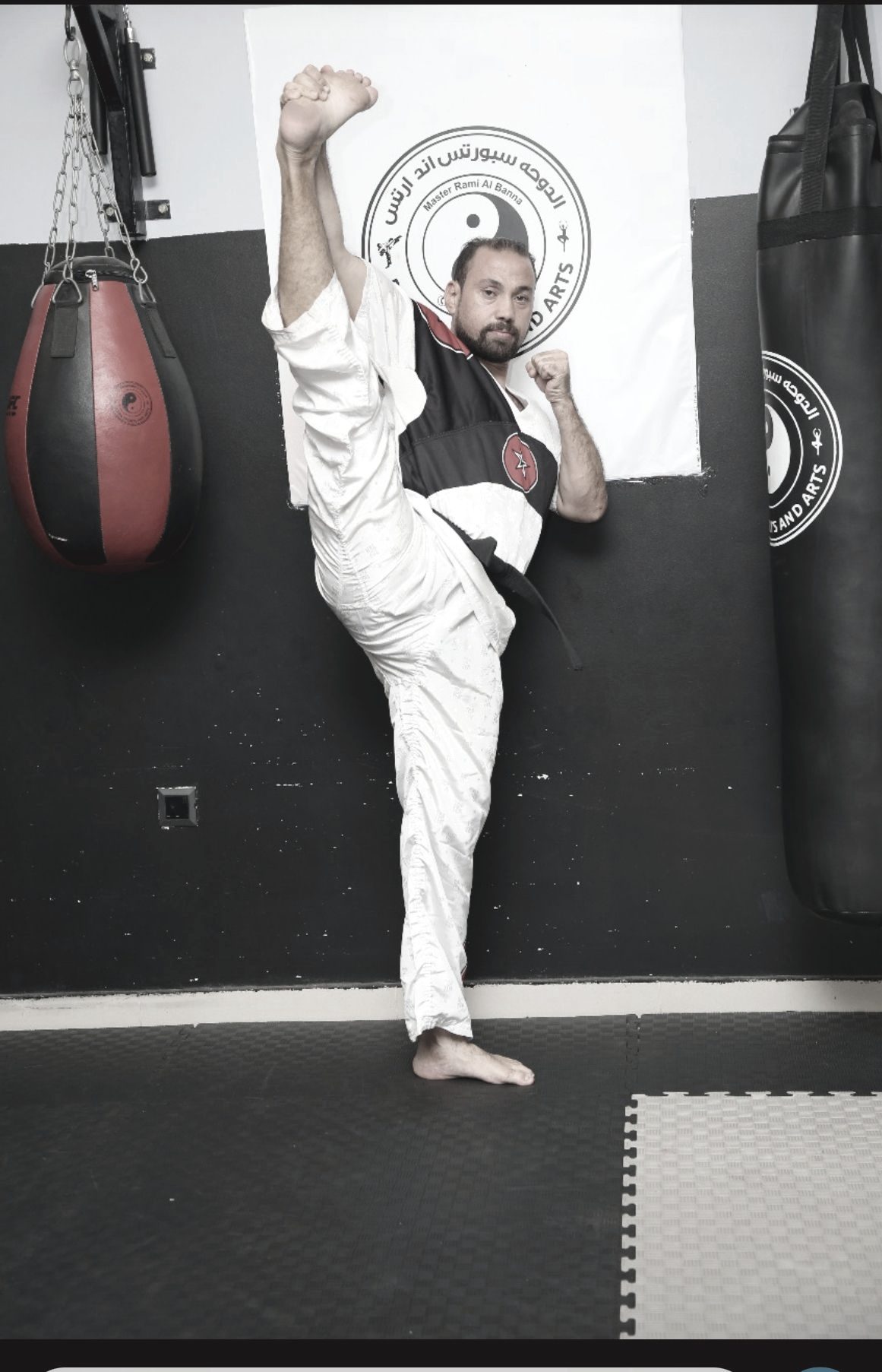 Master Rami Al Banna captured mid high kick in fighting stance, a club banner visible behind him.