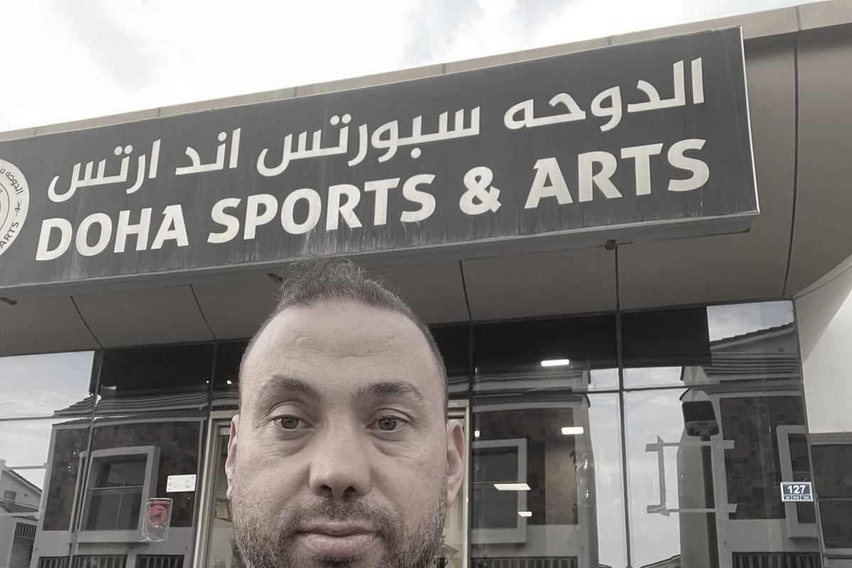 The Doha Sports and Arts sign, in Arabic and English, running the full width of the club's glass front, with Master Rami Al Banna standing under it.