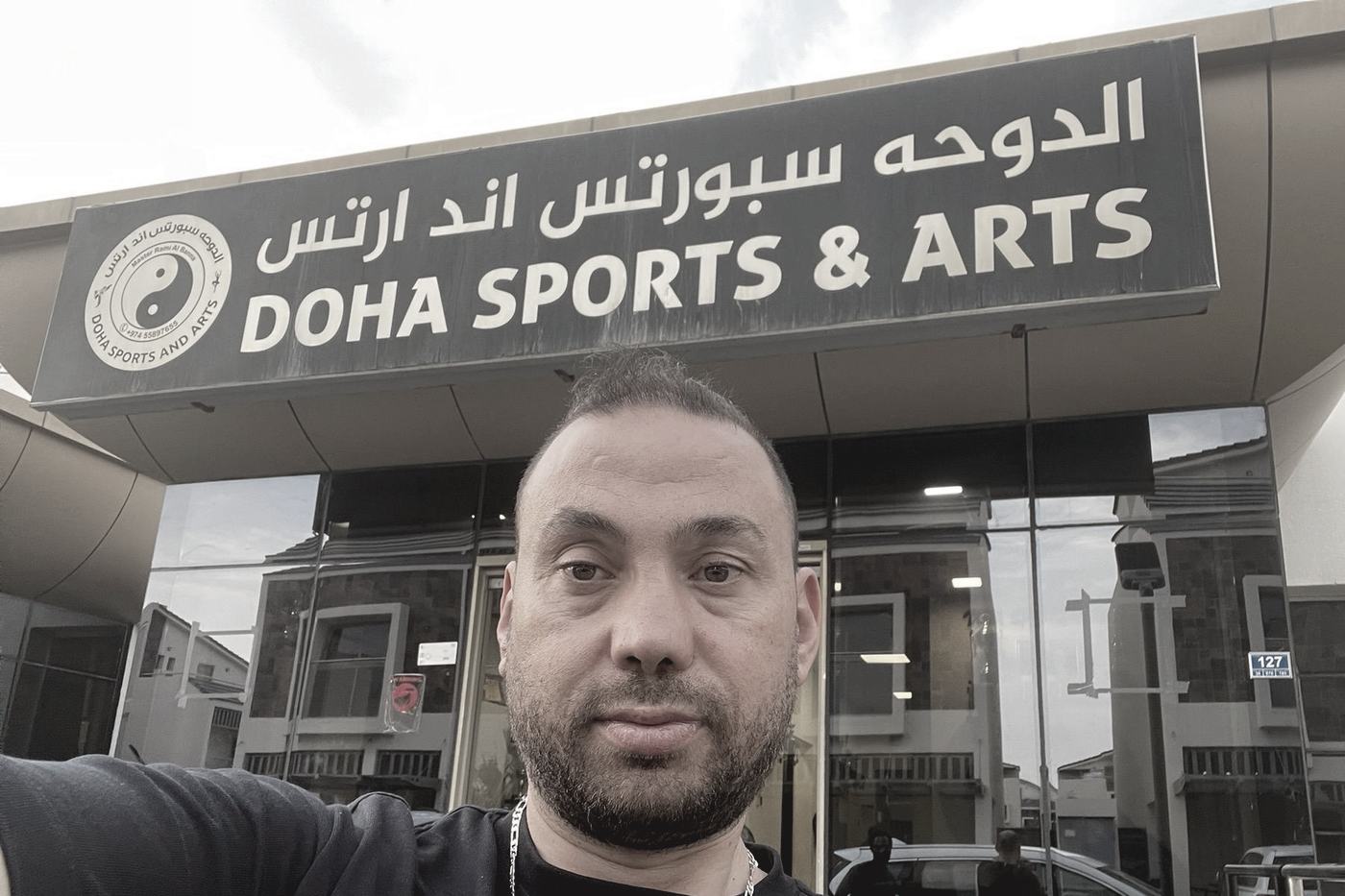 The Doha Sports and Arts sign in Arabic and English above the glass front of the club, with Master Rami Al Banna standing under it.
