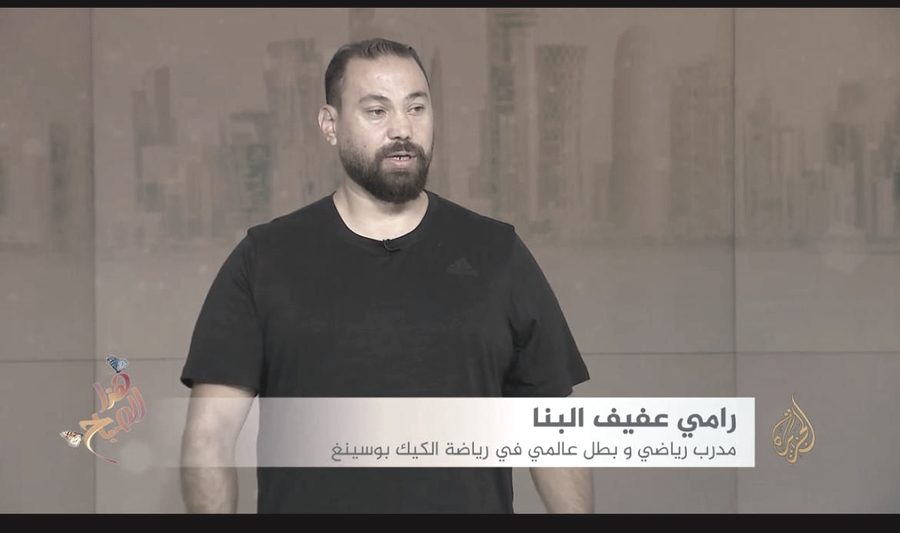 A television still of Rami Al Banna during an interview, the lower third naming him as a coach and former world champion in kickboxing.